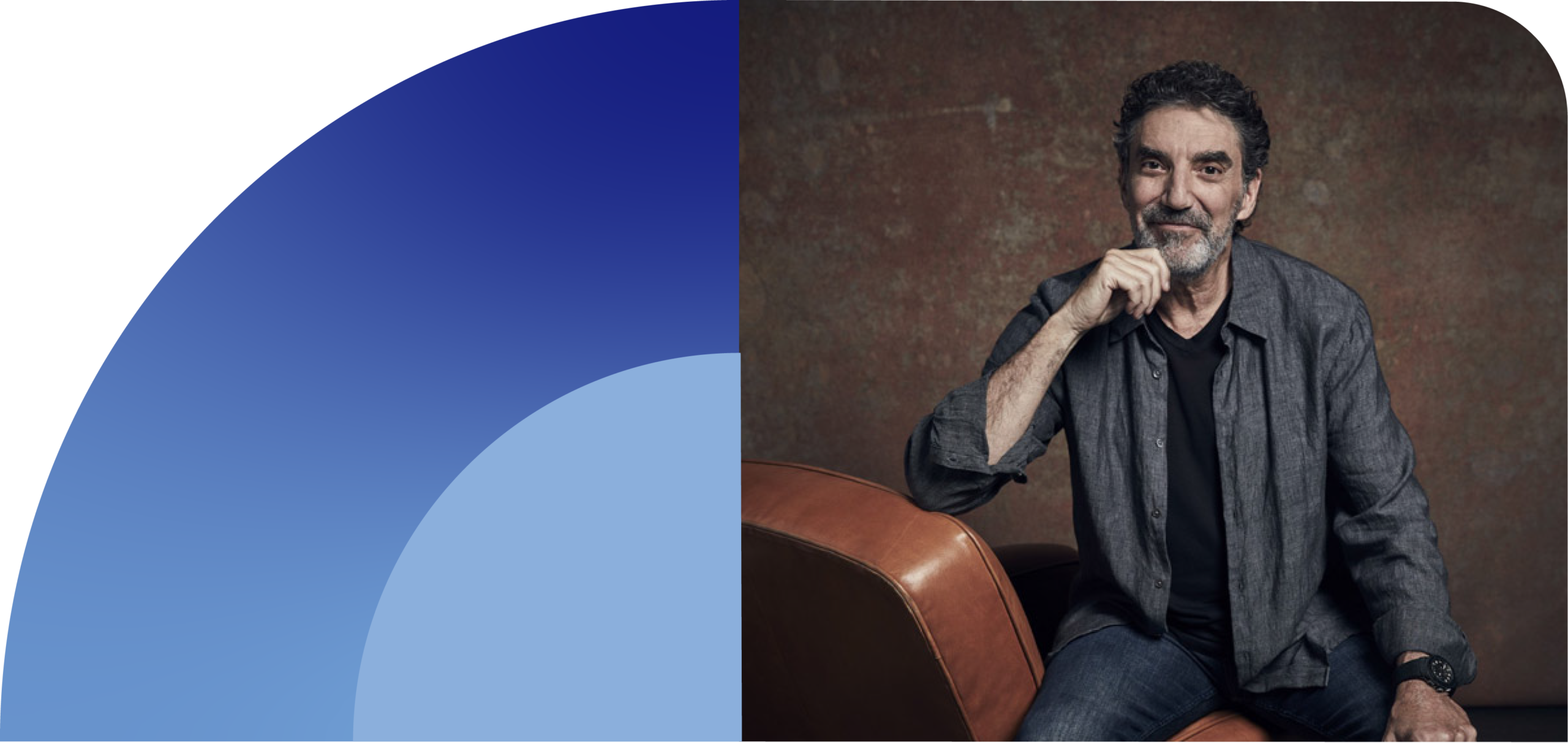 A Man With Curly Dark Hair And A Beard Sits On A Brown Leather Chair, Wearing A Dark Shirt And Jacket, Resting His Chin On His Hand, Against A Textured Brown Background. Blue Curved Shapes Are On The Left Side Of The Image.